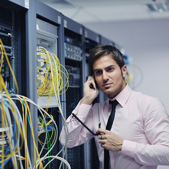 Male network administrator talks on phone next to computer servers