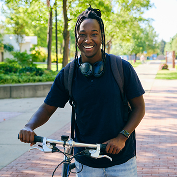 A student walking his bicycle on campus